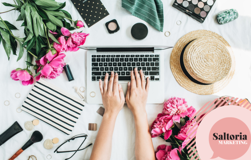 saltoria person typing on a laptop surrounded by decorative items like flowers, a summer hat and stationary.