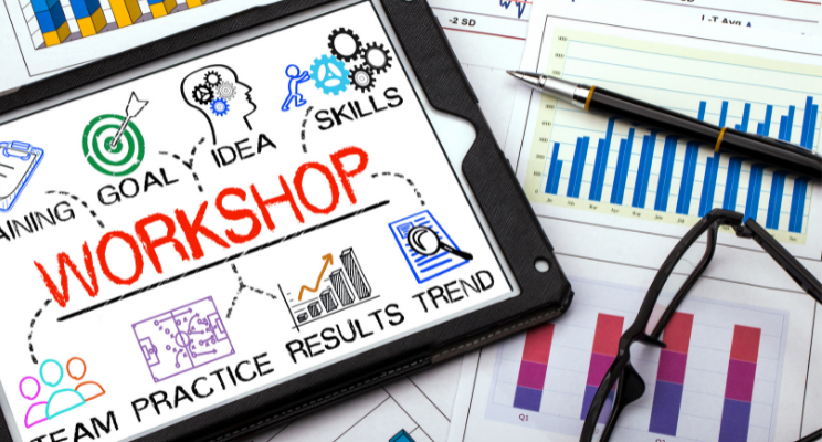 A display of an ipad and stationary with the word 'workshop' on the ipad and illustrations like graphs & team icons.