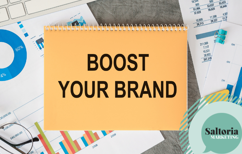 saltoria Picture of a notebook on a desk. There's a sentece written on the hard cover of the notepad that reads 'boost your brand'