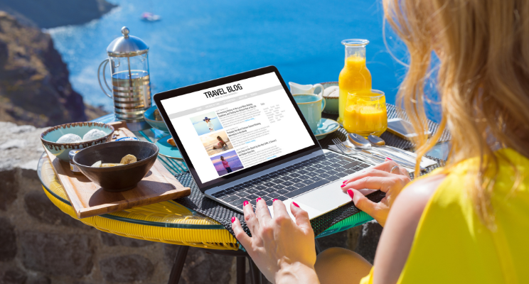 blonde lady writing a travel blog beside the sea